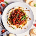 Overhead view of bruschetta dip topped with cherry tomatoes, basil, and balsamic glaze, surrounded by slices of bread.