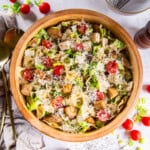 Large wooden bowl filled with pasta salad, topped with shredded Parmesan and croutons.