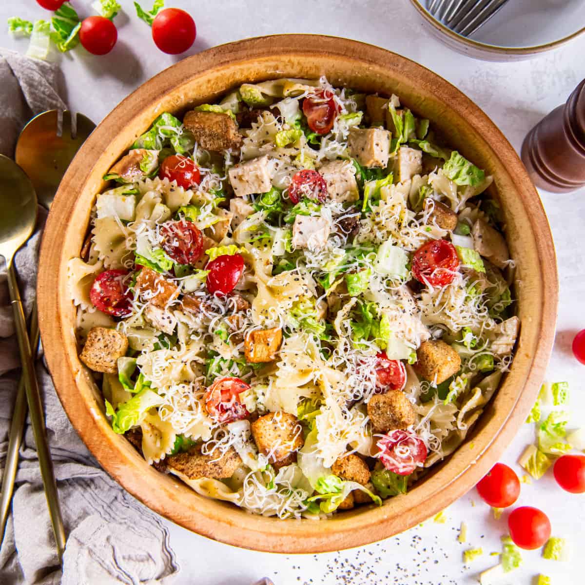 Large wooden bowl filled with pasta salad, topped with shredded Parmesan and croutons.