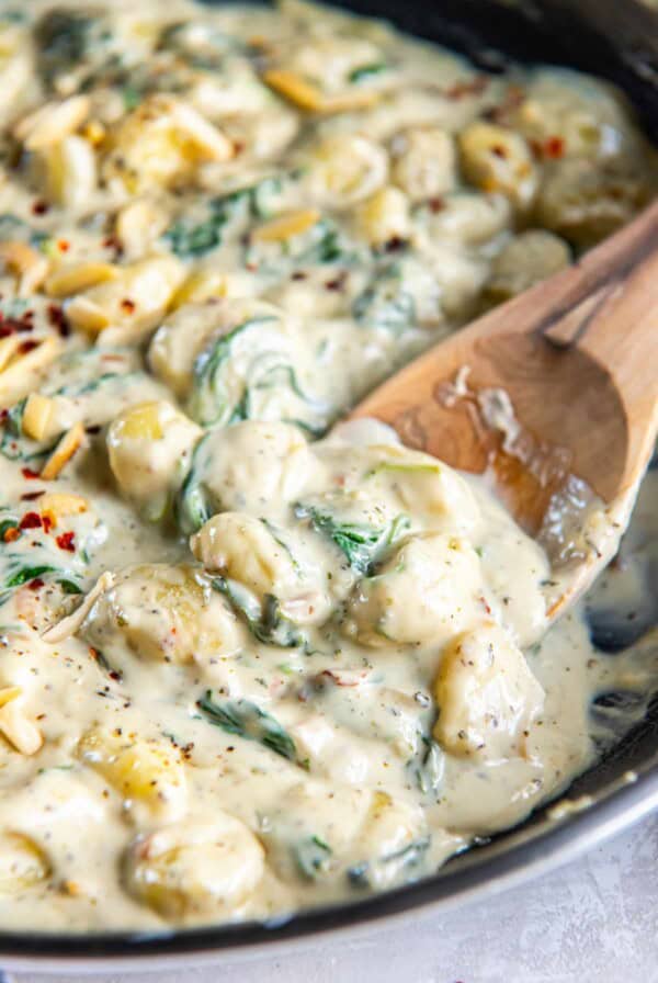 Close-up of gnocchi coated in creamy gorgonzola sauce with spinach and cheese with wooden spoon.