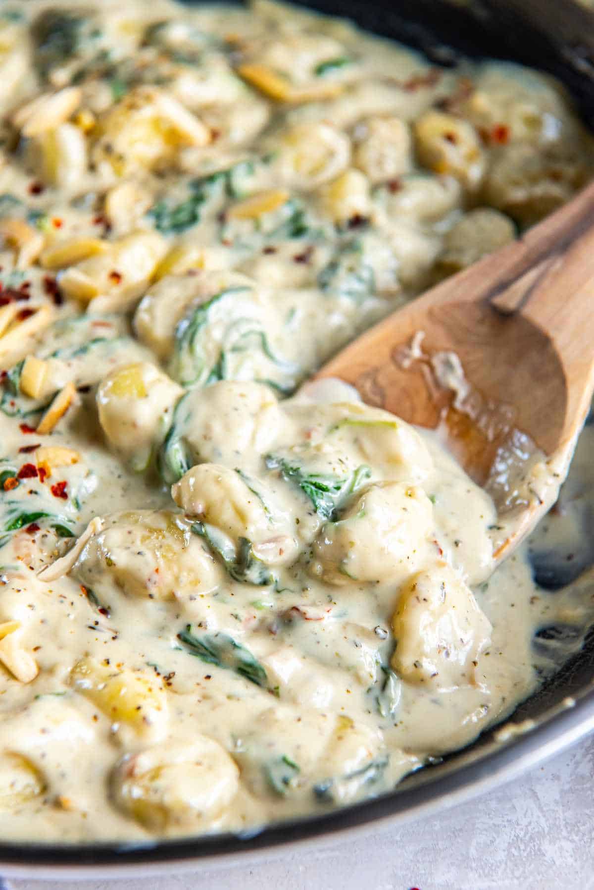 Close-up of gnocchi coated in creamy gorgonzola sauce with spinach and cheese with wooden spoon.