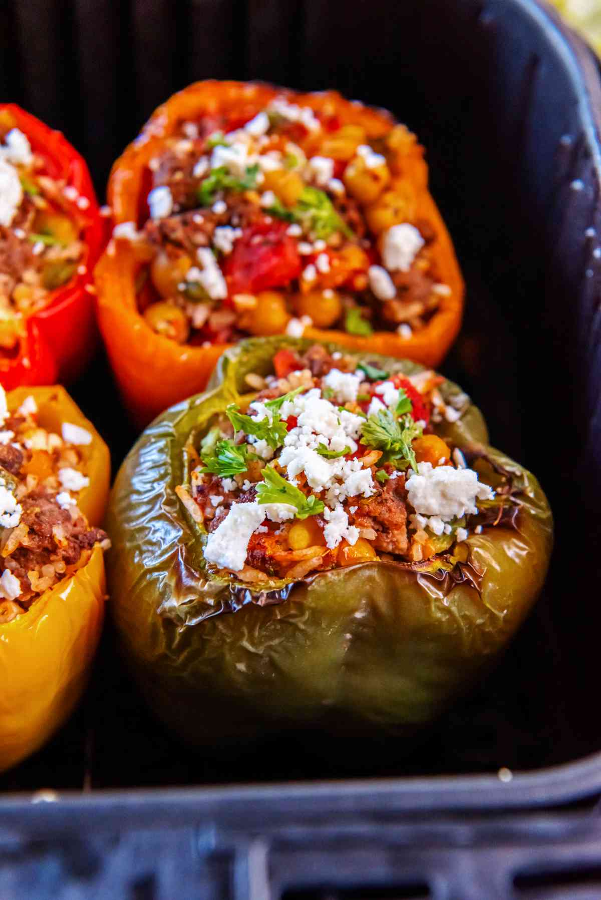 Close-up of cooked Greek stuffed peppers in an air fryer, filled with a savory mixture of beef, rice, chickpeas, and herbs, finished with crumbled feta.