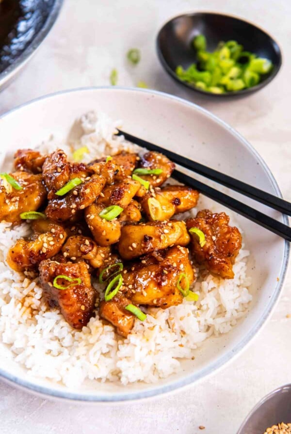Side view of honey butter chicken in a bowl with chopsticks and scallions on the side, ready to serve.