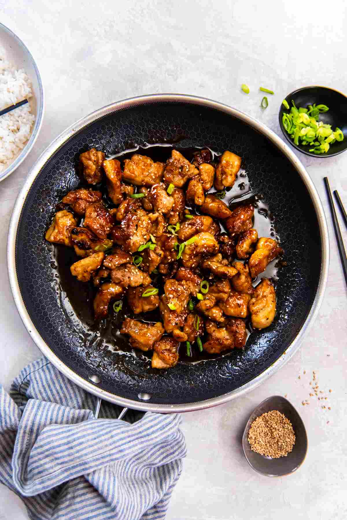 Overhead shot of honey butter chicken in a skillet, garnished with sesame seeds and sliced green onions.