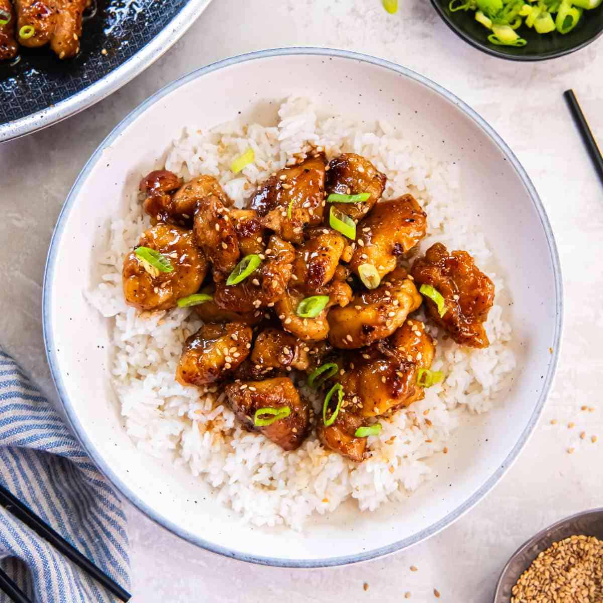 Bowl of honey butter chicken served over white rice, topped with sesame seeds and green onions.