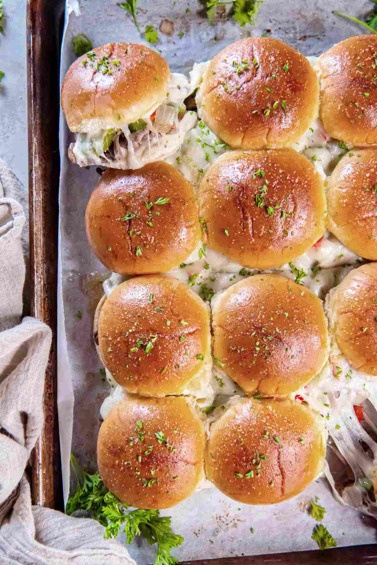 Overhead view of golden brown baked sliders topped with parsley.