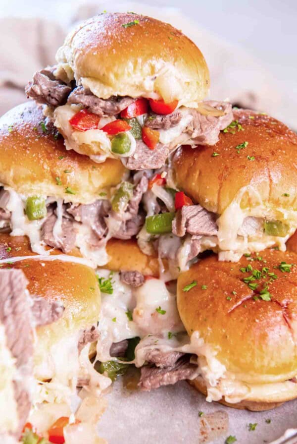 Stack of warm cheesesteak sliders with melted cheese and diced peppers.