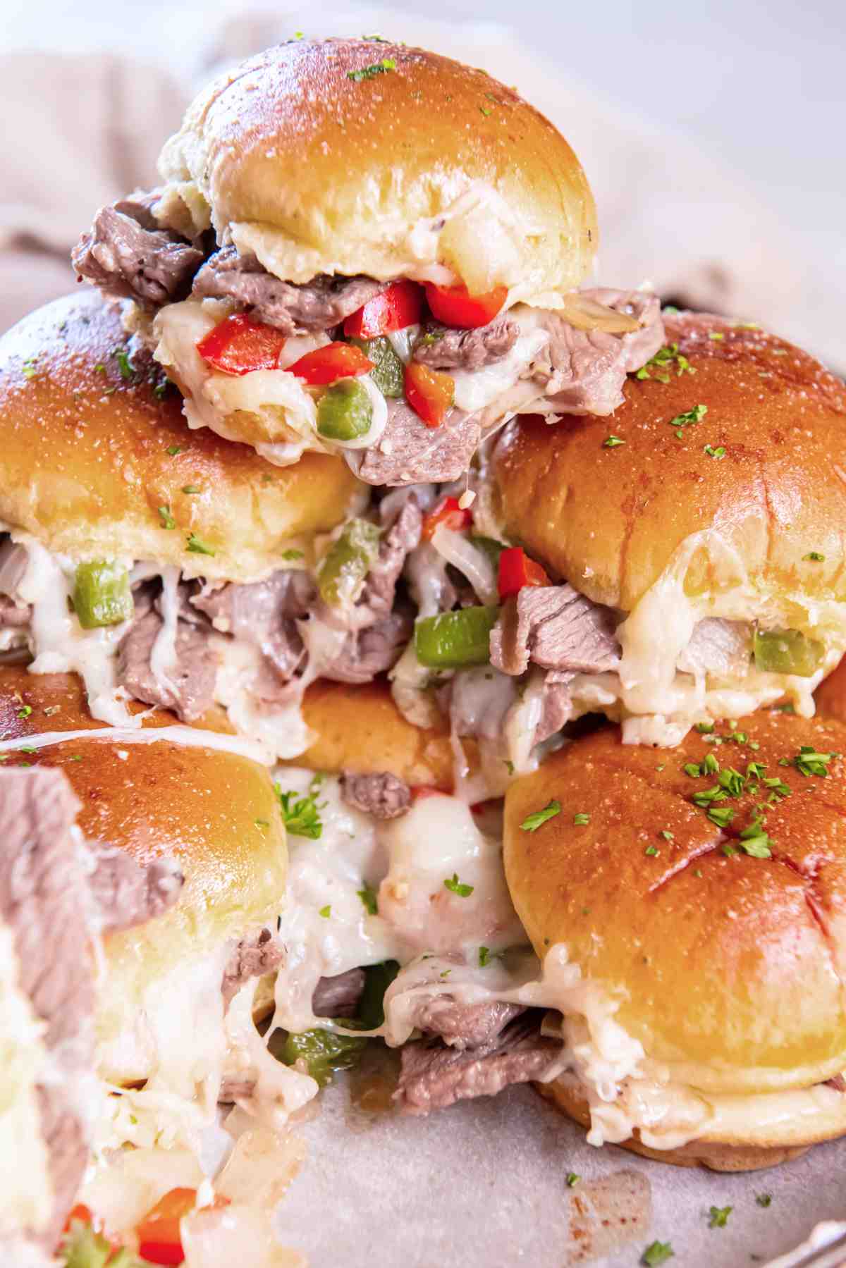 Stack of warm cheesesteak sliders with melted cheese and diced peppers.