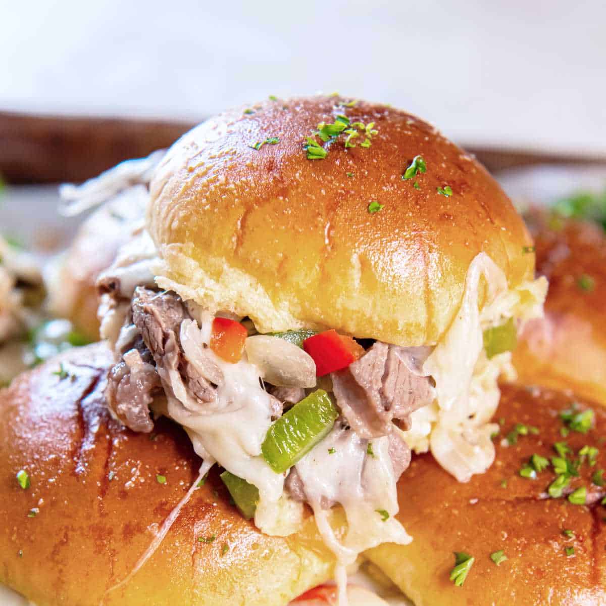 Close-up of a cheesesteak slider showing melted cheese, peppers, and steak inside the bun.