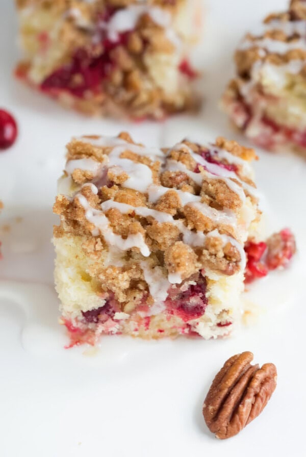 Close up of a square of cranberry crumb cake topped with sweet vanilla glaze and crunchy crumb topping.