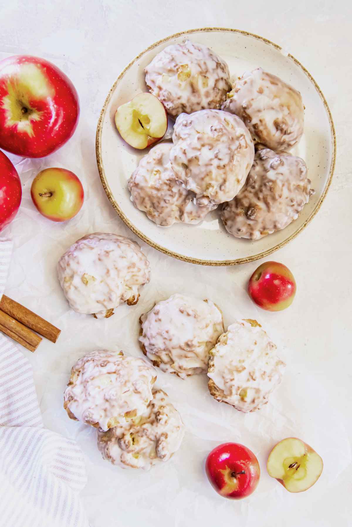 Overhead view of glazed air fryer applesauce fritters on a plate with fresh apples and cinnamon sticks, showing their golden brown texture and soft apple pieces.
