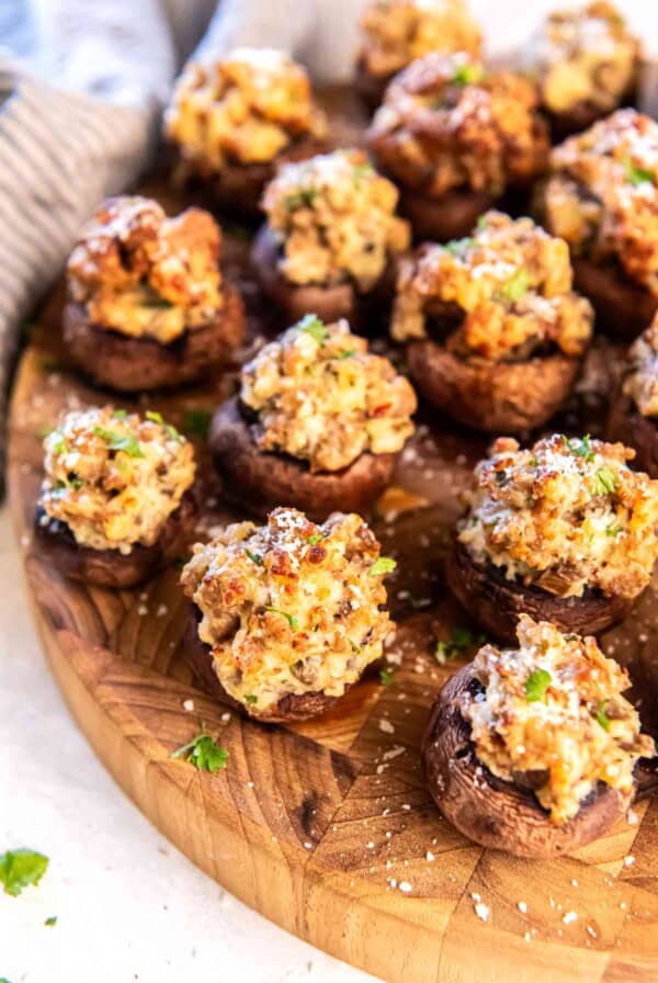 Golden brown sausage stuffed mushrooms arranged on a wooden board, garnished with parsley and grated Parmesan.