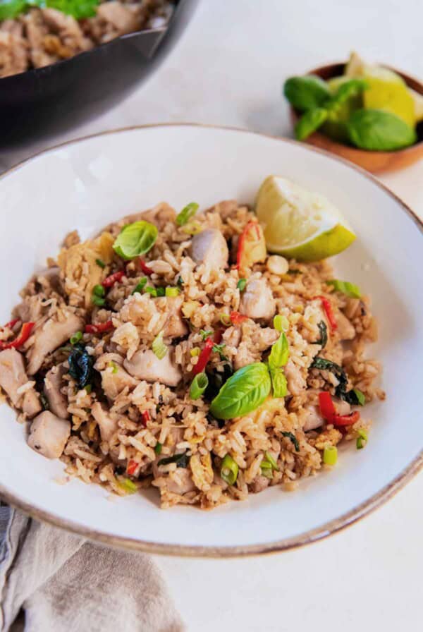 Angle view of Thai Basil Fried Rice with tender chicken pieces, basil, chilies, and green onions in a white bowl.