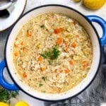 Turkey and rice soup simmering in a Dutch oven with fresh herbs on top.
