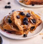 Slice of blueberry brioche French toast bake topped with blueberries, powdered sugar, and maple syrup