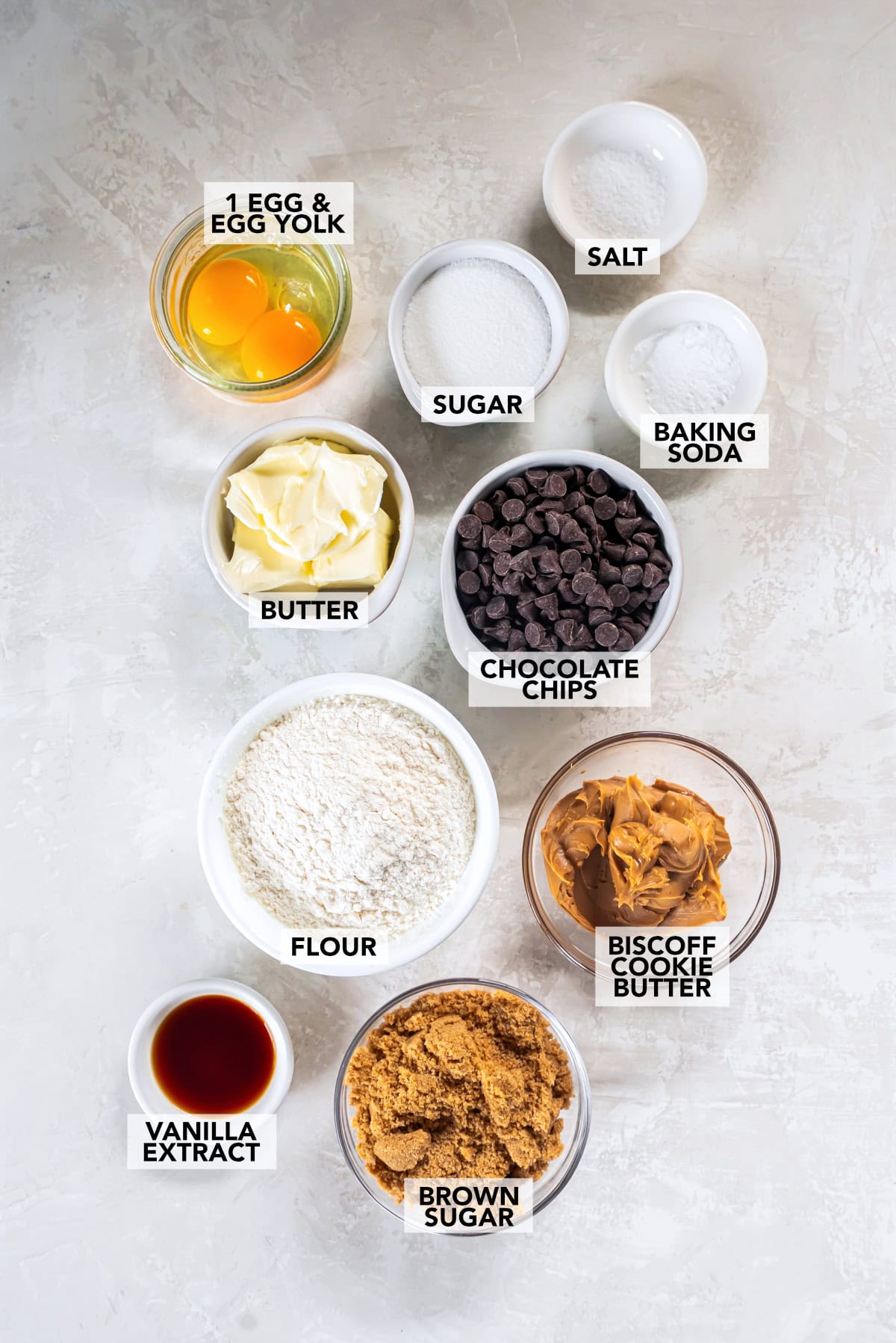 ingredients on a table including cookie butter, flour, egg, egg yolk, sugar, brown sugar, salt, baking soda, vanilla extract, and butter. 