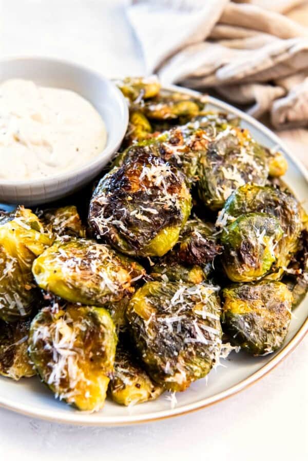 Plated smashed Brussels sprouts topped with parmesan cheese served with aioli dipping sauce
