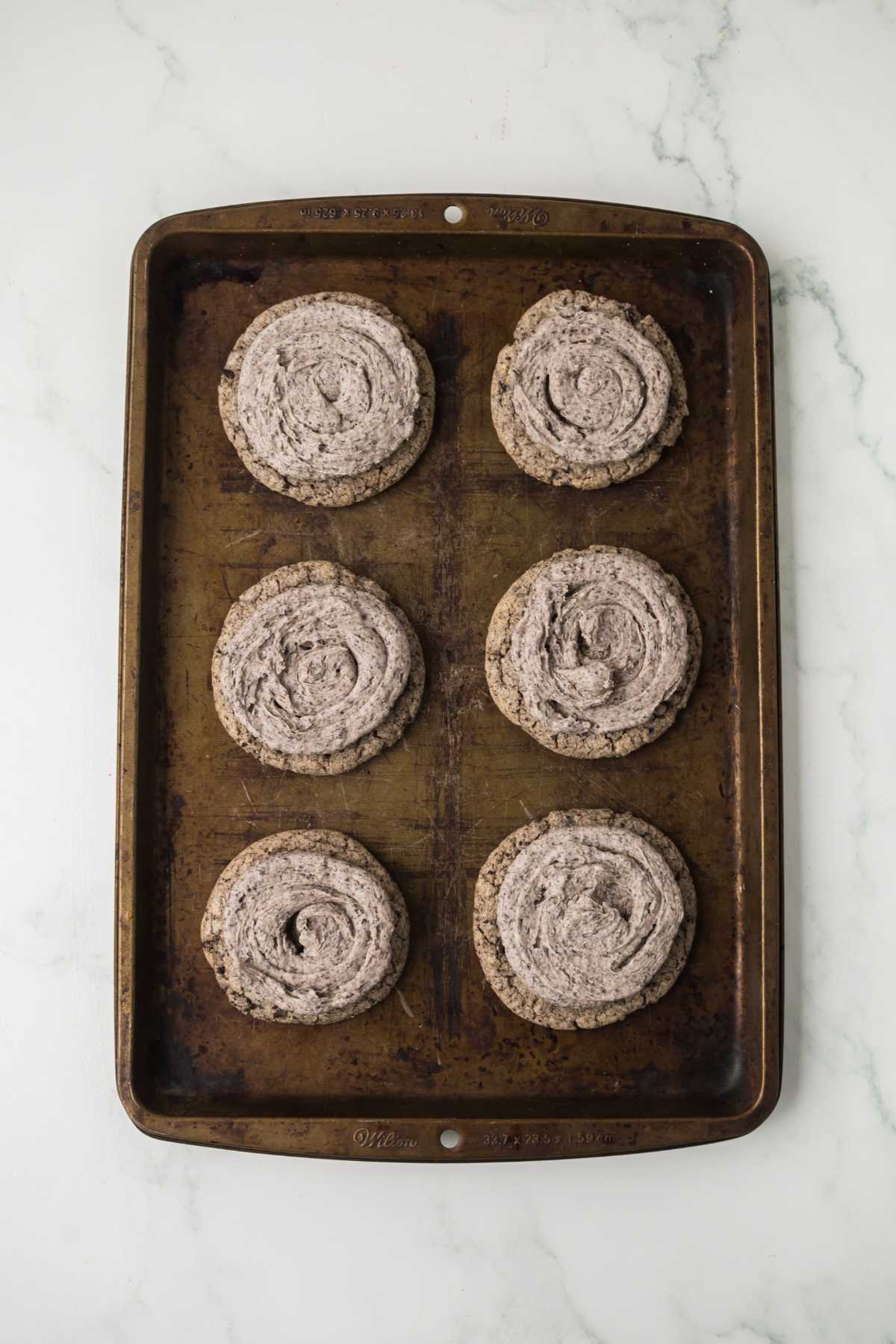 Oreo Milkshake Cookies topped with swirls of cookies-and-cream buttercream frosting on a baking sheet.