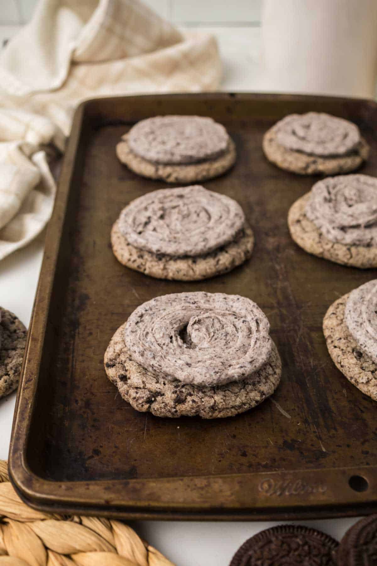 Close view of frosted Oreo Milkshake Cookies on a rustic baking sheet.