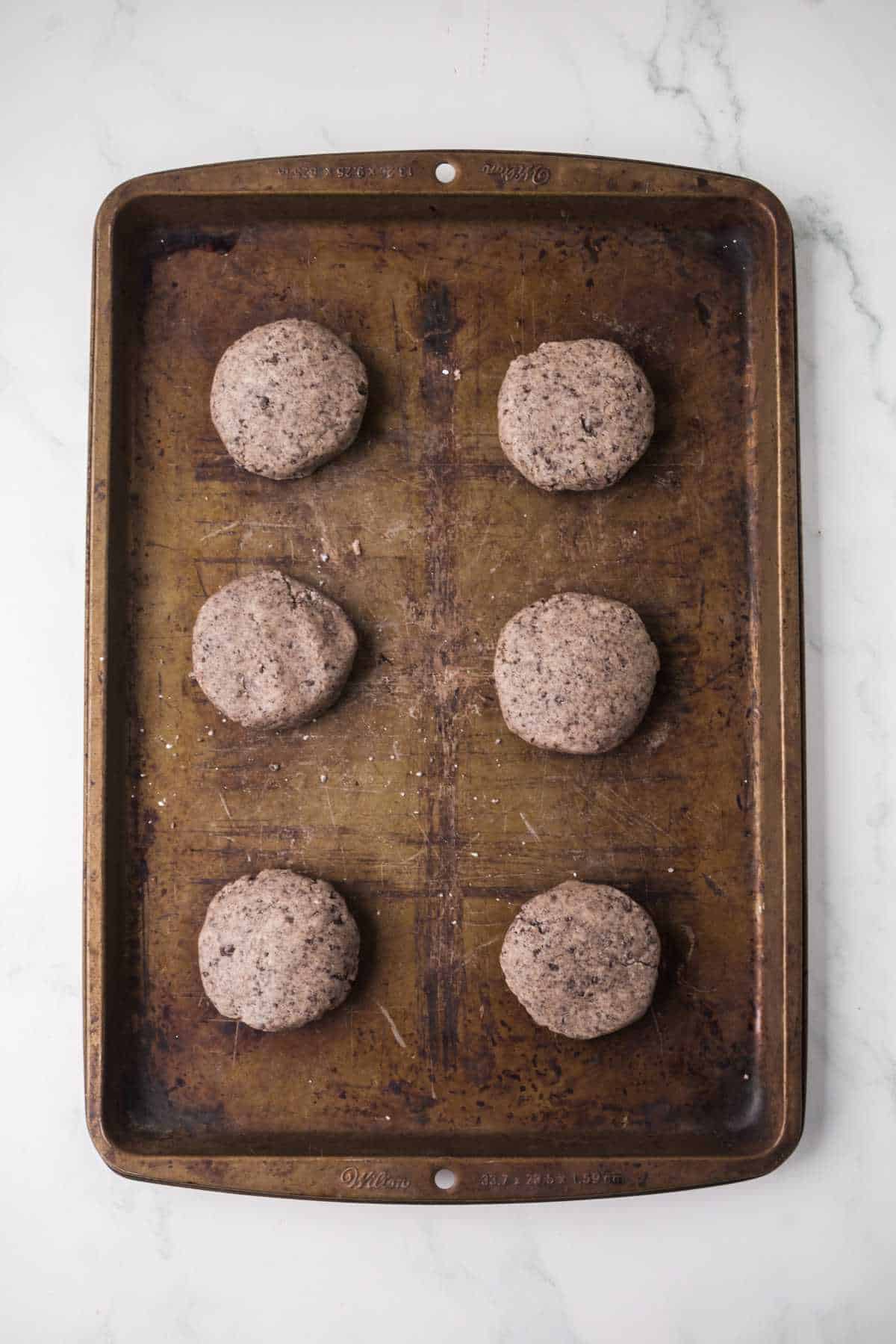Scooped Oreo cookie dough shaped into thick discs on a baking sheet before chilling and baking.