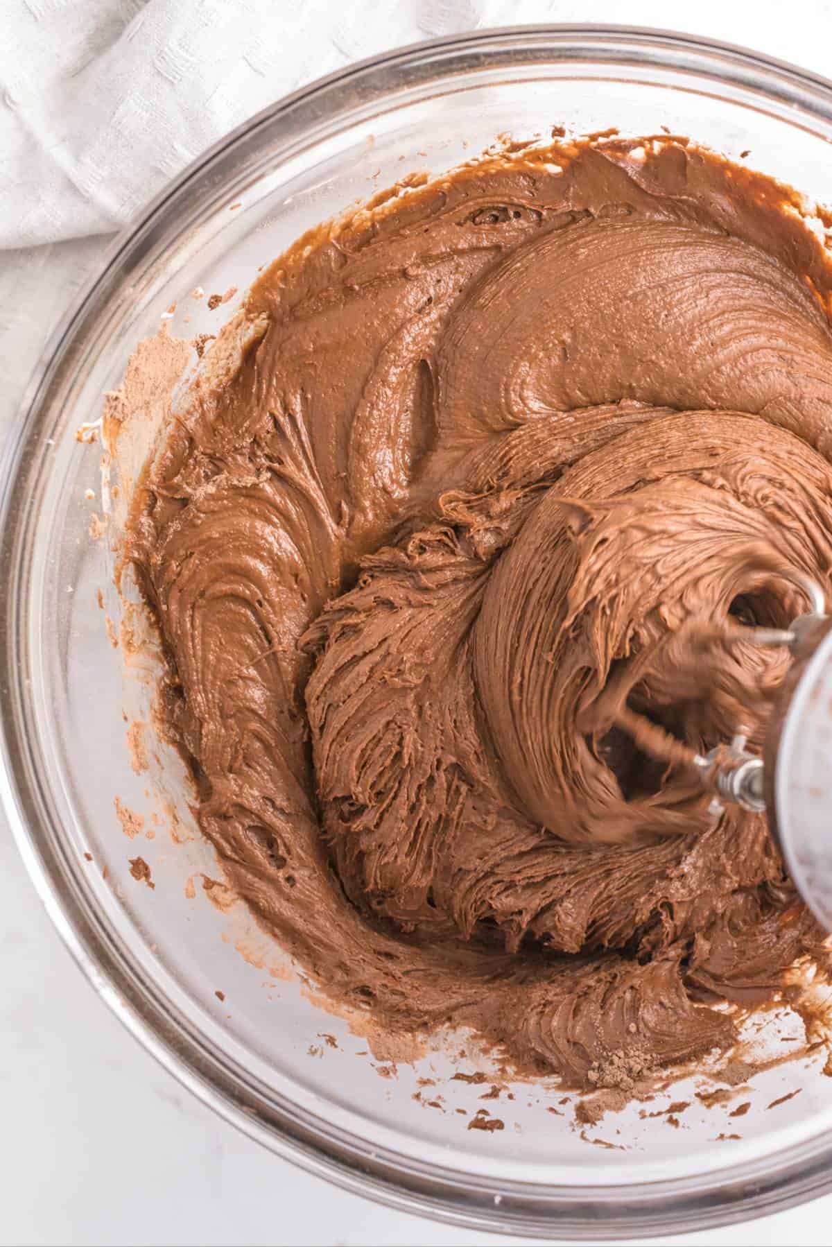 Mixing chocolate cupcake batter in a glass bowl with a hand mixer