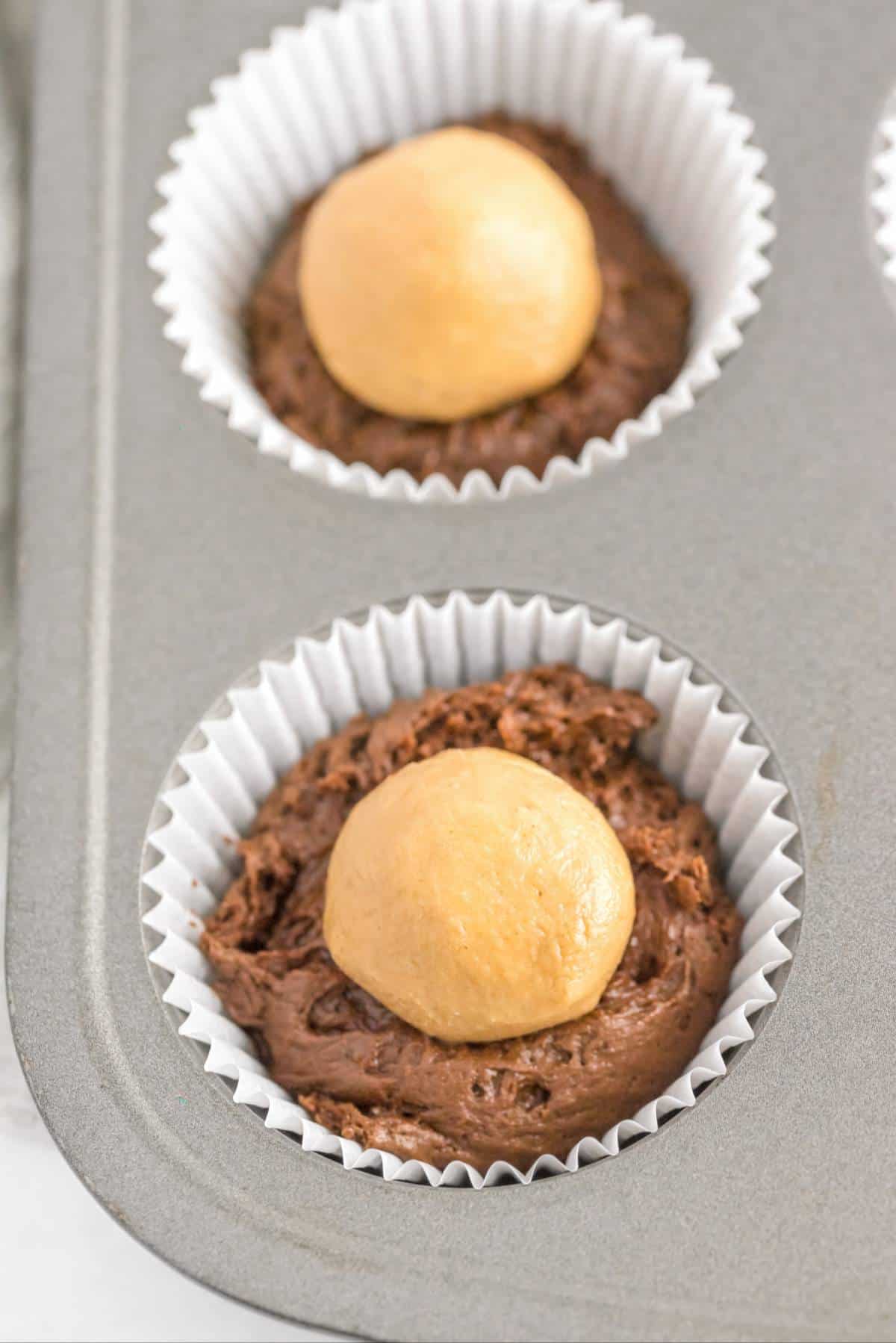 Chocolate cupcake batter filled with a ball of peanut butter filling in a cupcake liner
