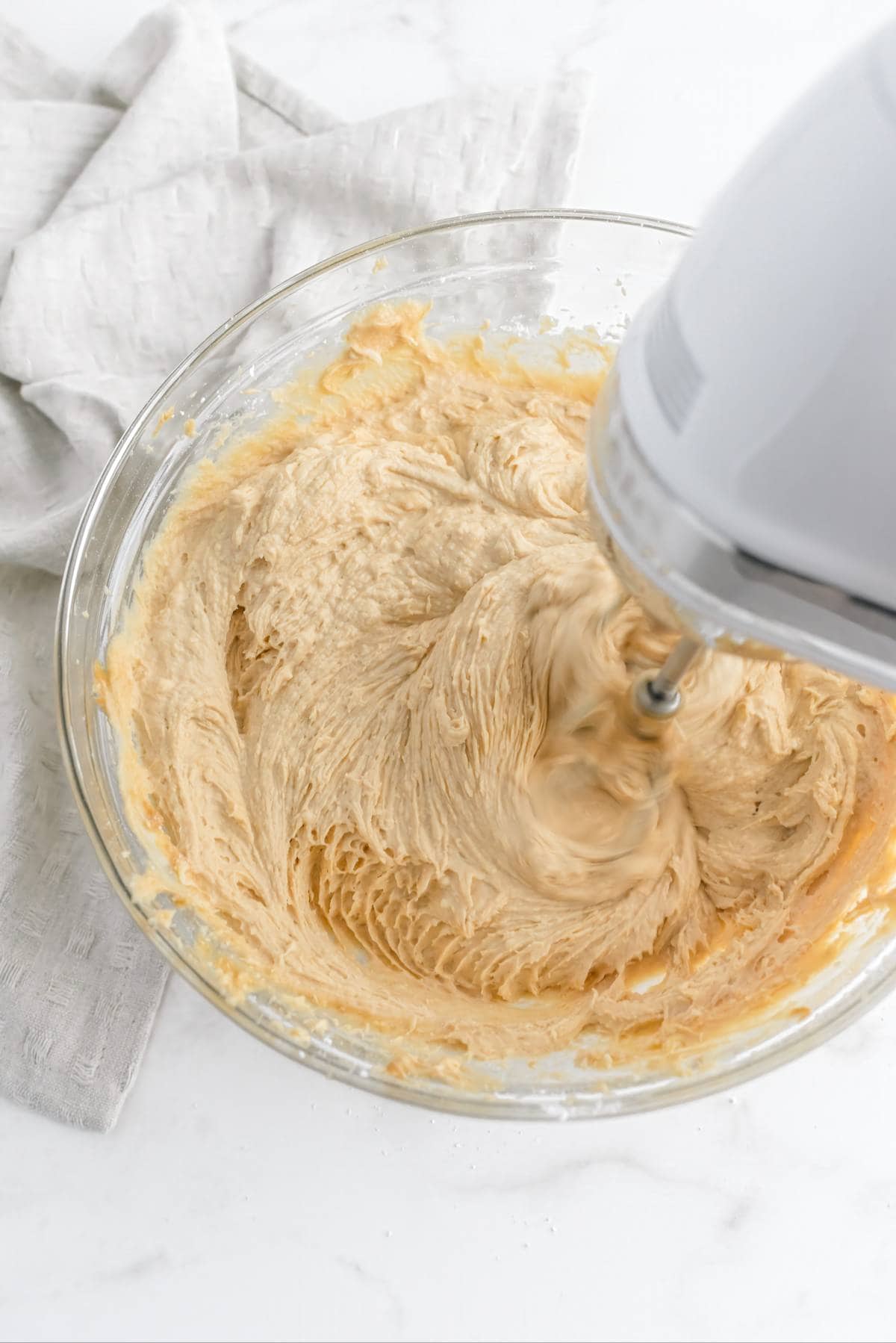Mixing creamy peanut butter frosting in a glass bowl with a hand mixer