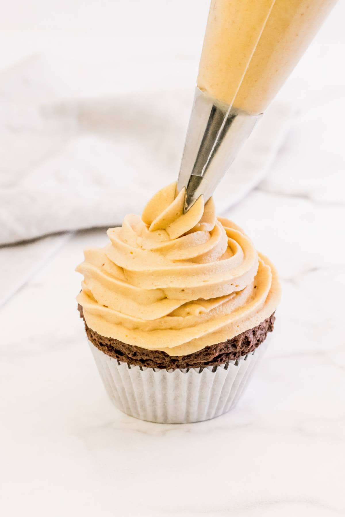 Piping peanut butter frosting onto a chocolate cupcake