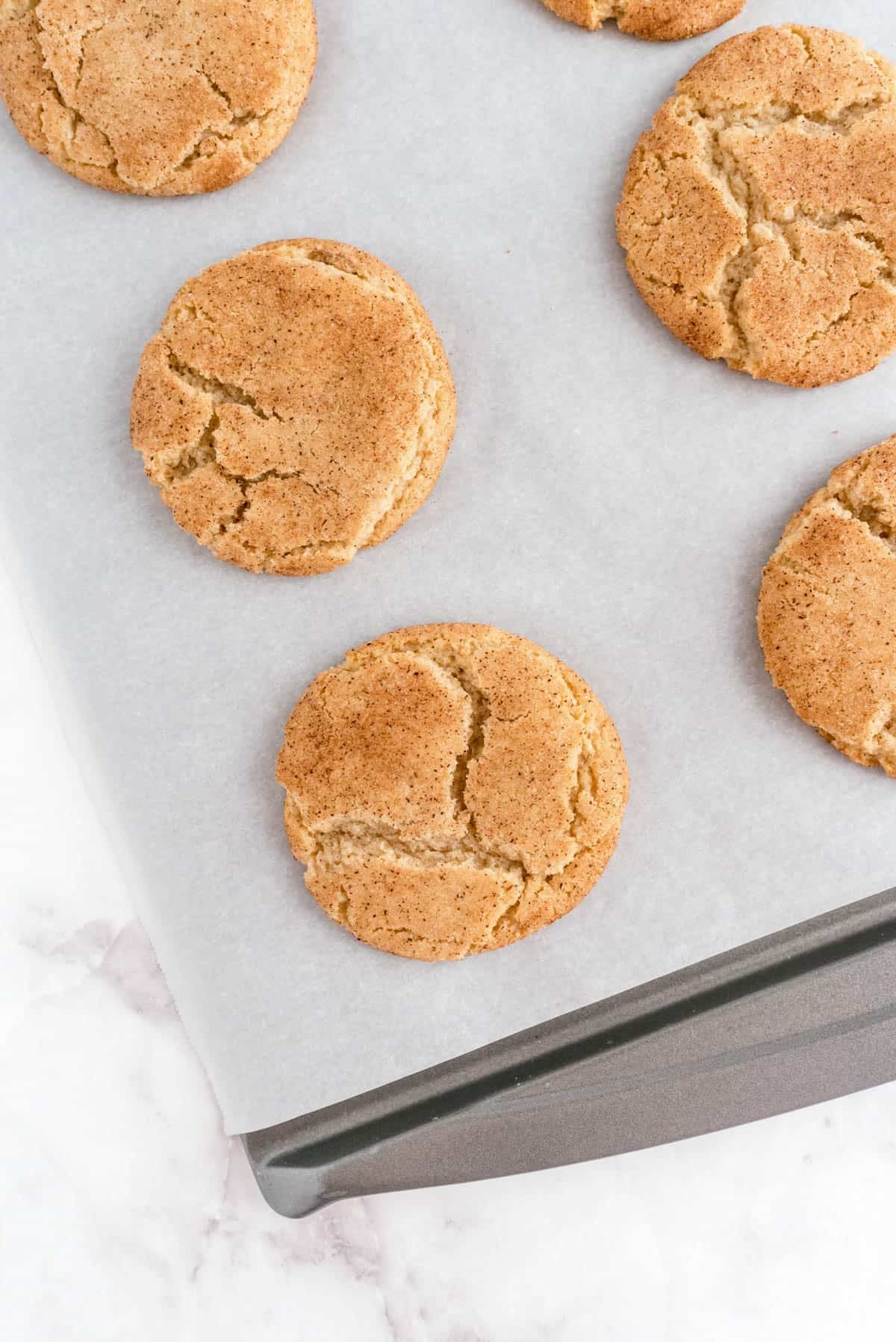 Brown butter snickerdoodle cookies baked on a parchment lined baking sheet with crackled tops
