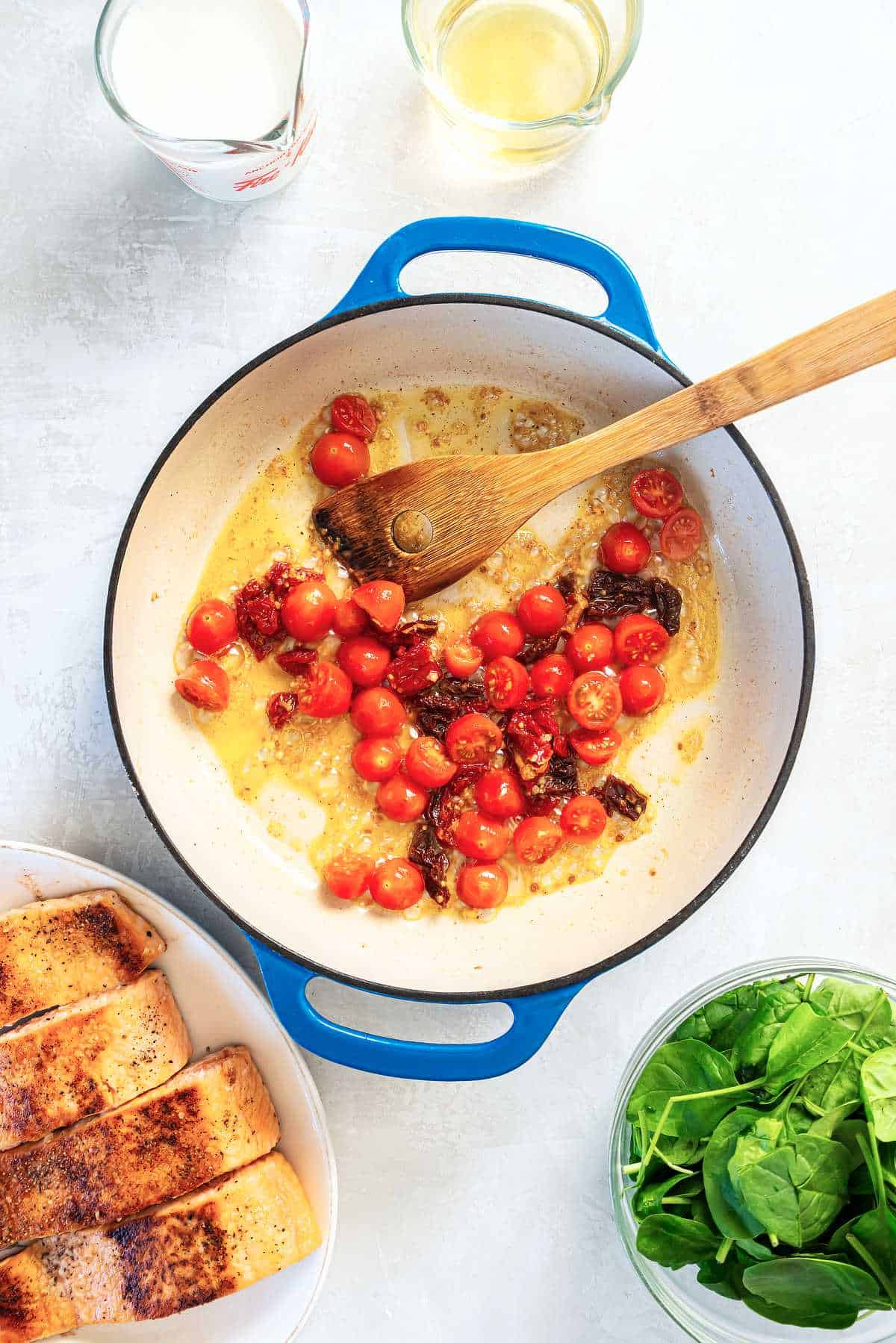 Cherry tomatoes and sun-dried tomatoes cooking in garlic butter to build flavor for Tuscan salmon sauce.