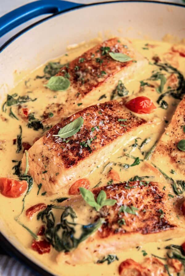 Pan-seared salmon simmering in a creamy Tuscan sauce with spinach and tomatoes in a skillet.