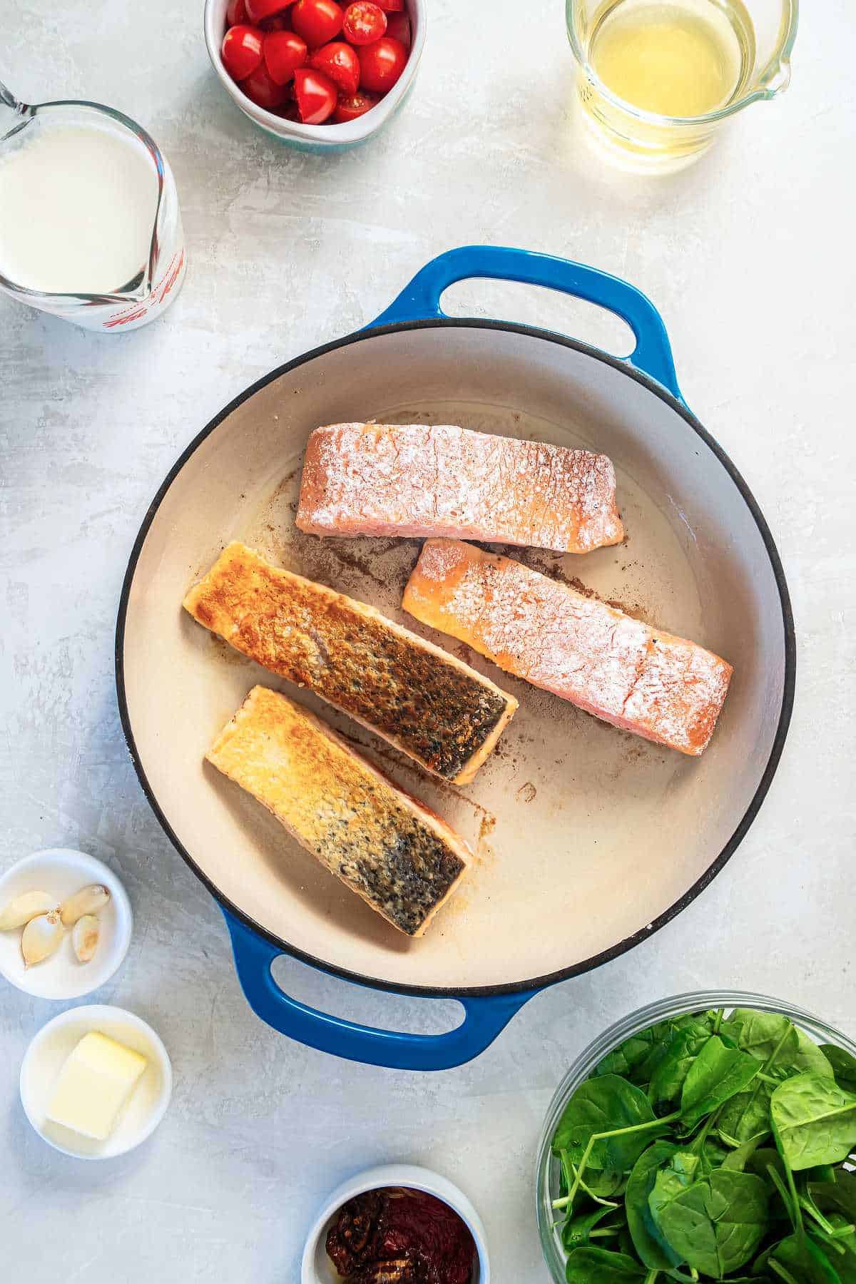 Salmon fillets searing in a skillet to create a golden crust for Tuscan salmon.