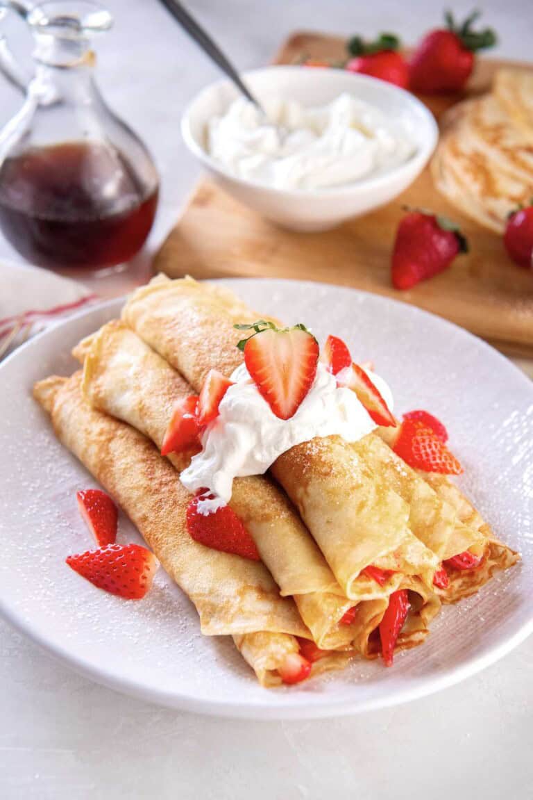 Easy pancake roll ups filled with strawberries and topped with whipped cream and powdered sugar on a plate