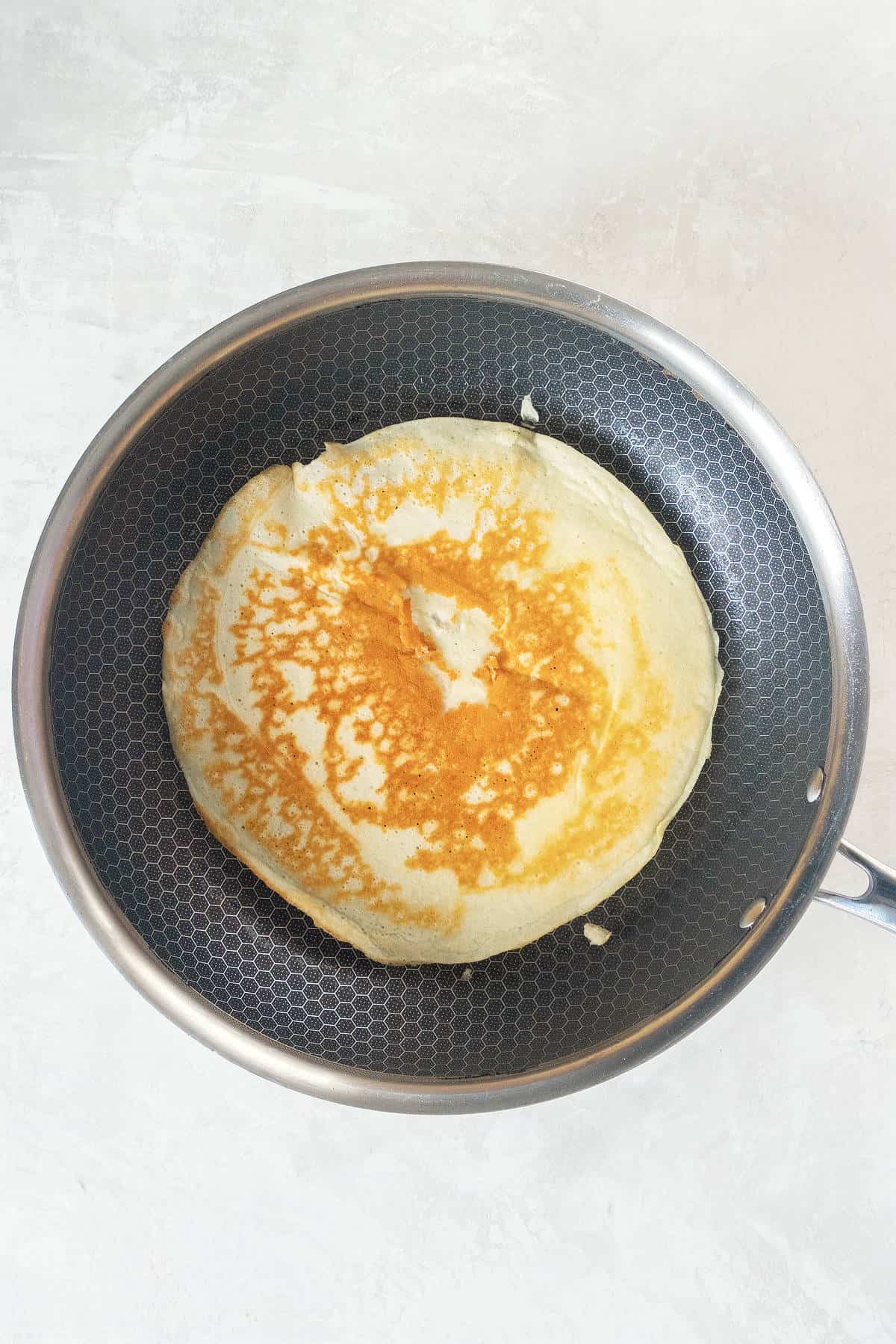 Thin pancake cooking in a skillet with light golden color for pancake roll ups
