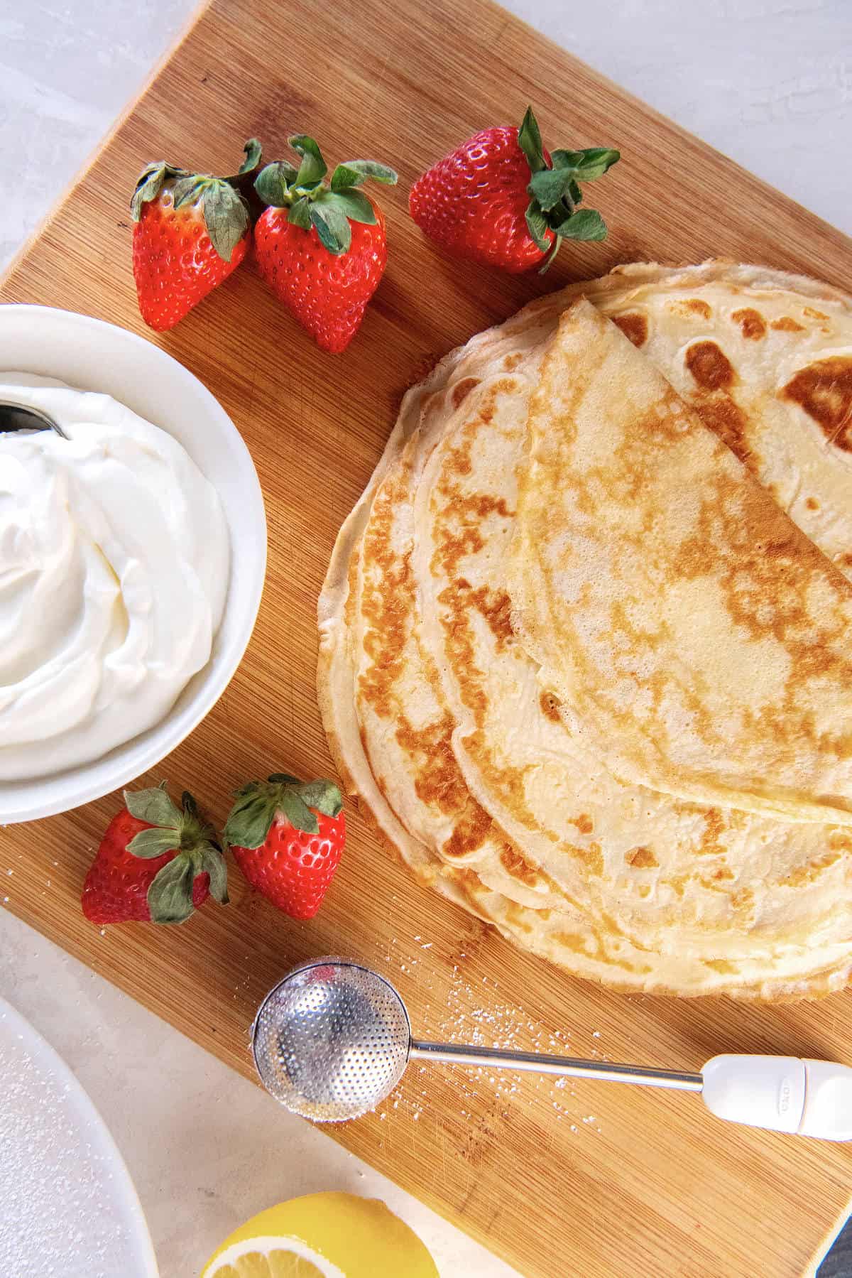 Thin pancakes on a board with strawberries and whipped cream ready for filling and rolling