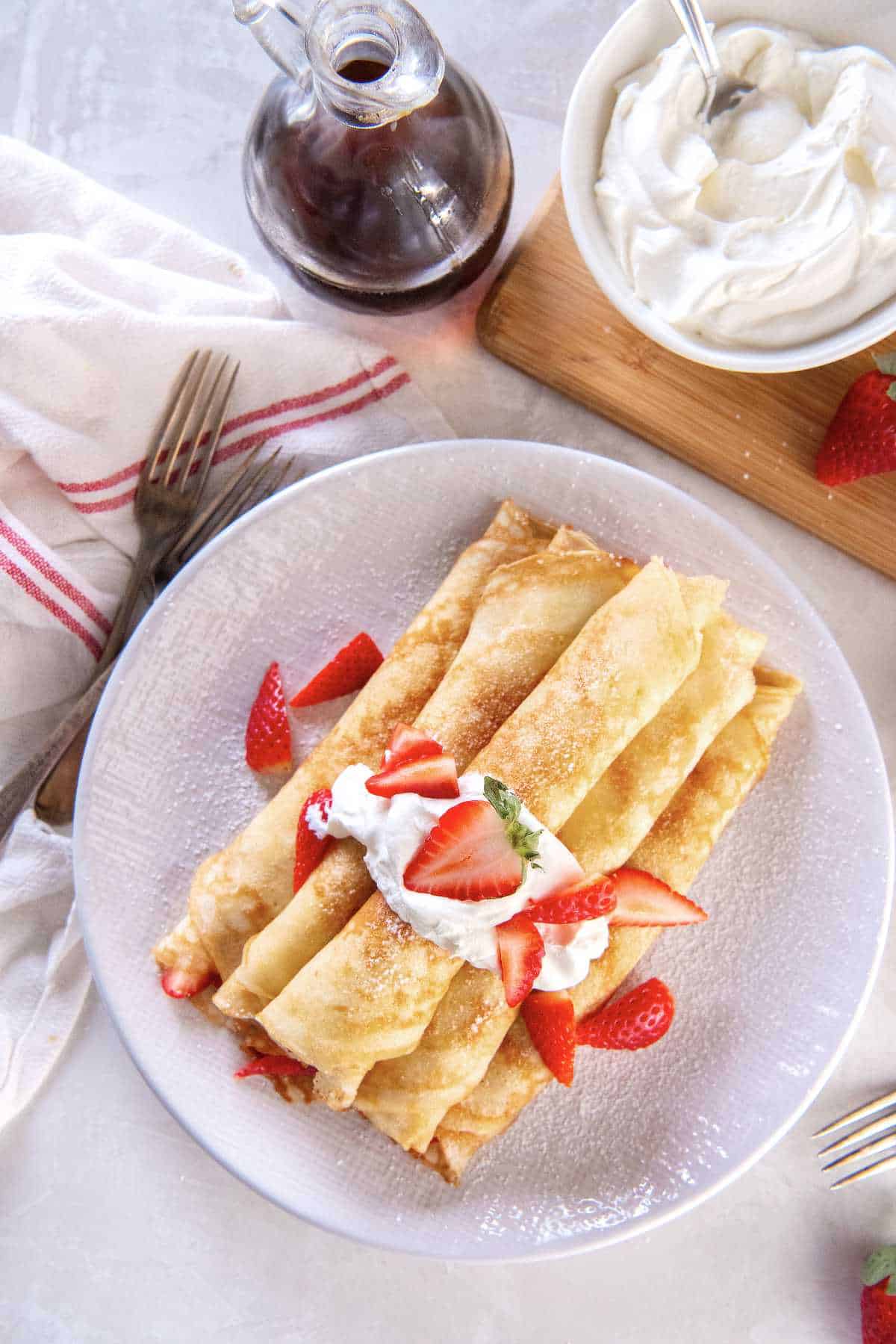 Thin pancake roll ups filled with fresh strawberries and topped with whipped cream and powdered sugar