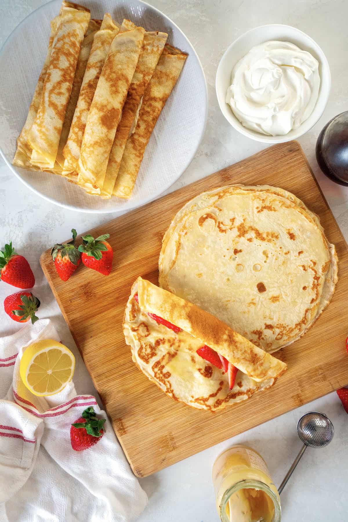 Thin pancakes on a cutting board being filled with strawberries and rolled into pancake roll ups