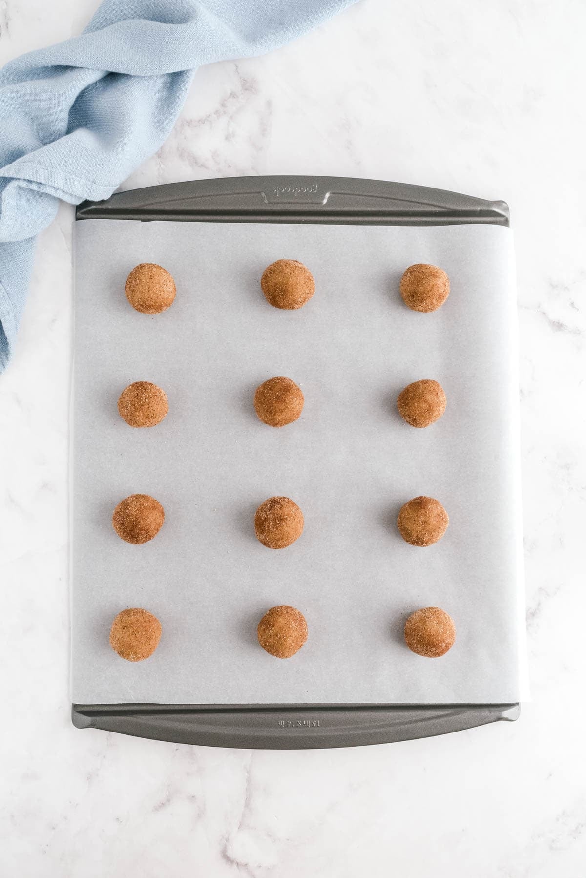 Cinnamon sugar coated snickerdoodle dough balls arranged on a parchment lined baking sheet