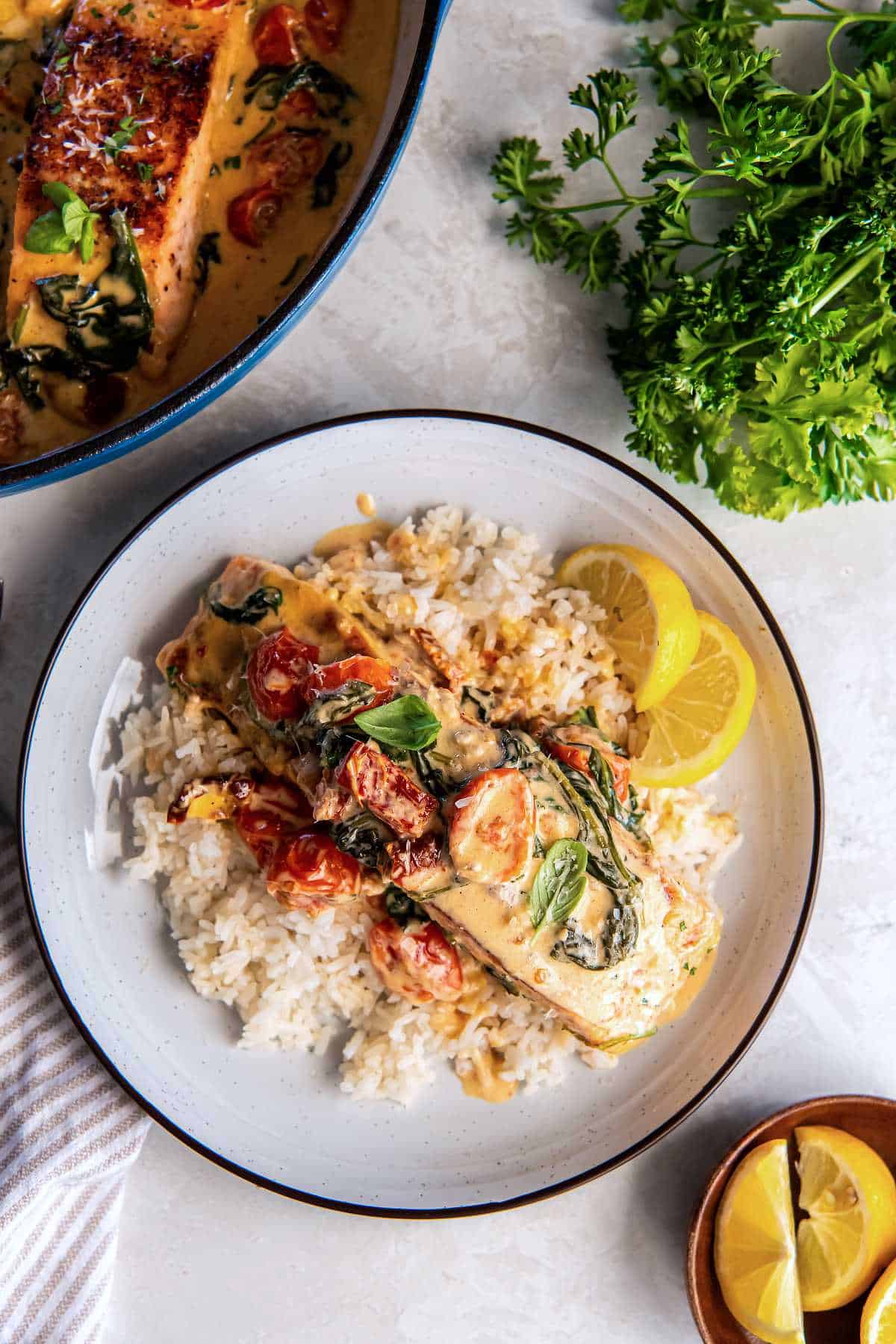 Creamy Tuscan salmon served over rice with spinach, tomatoes and lemon wedges.