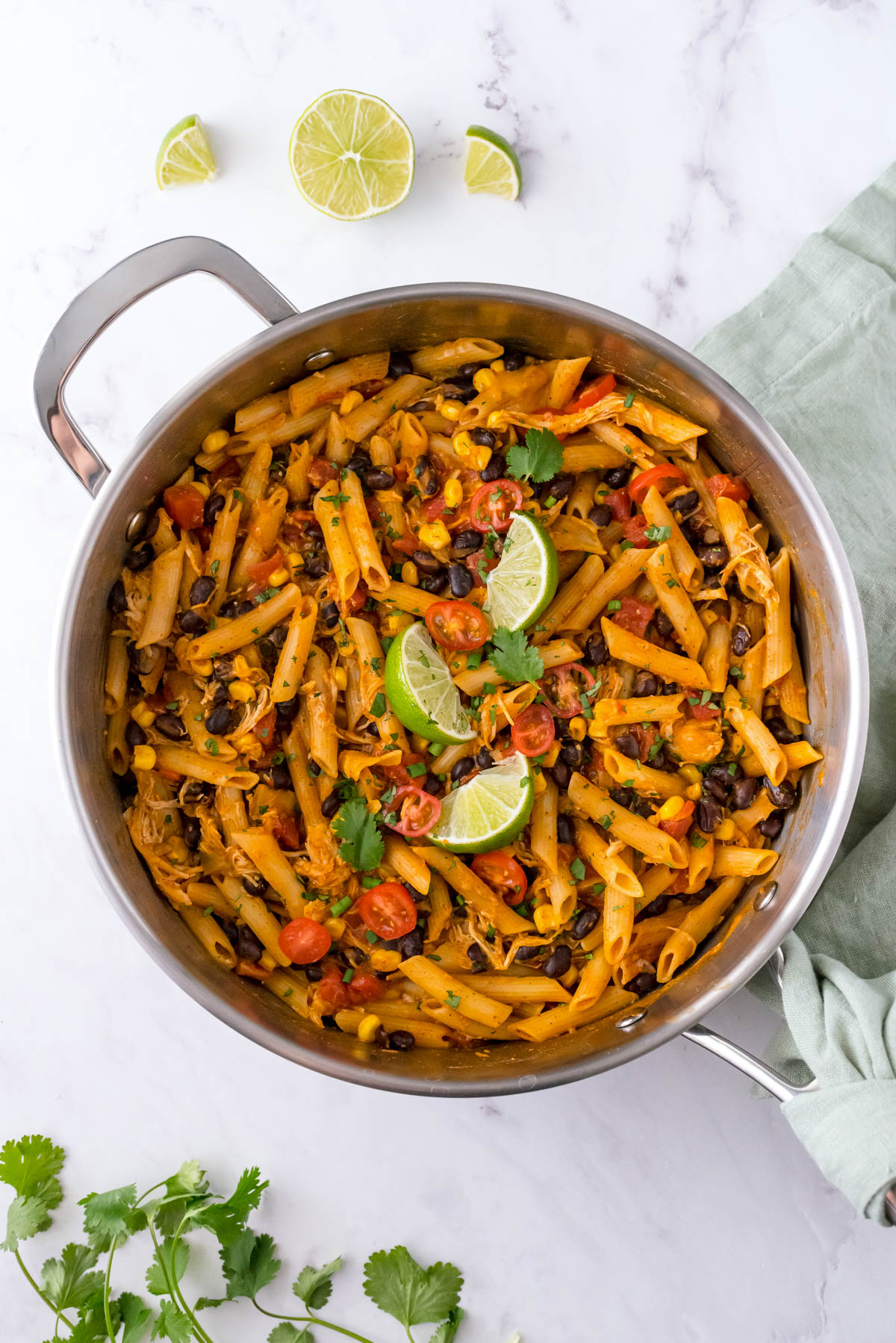 One pot chicken enchilada pasta in a skillet with black beans, corn, tomatoes and lime wedges