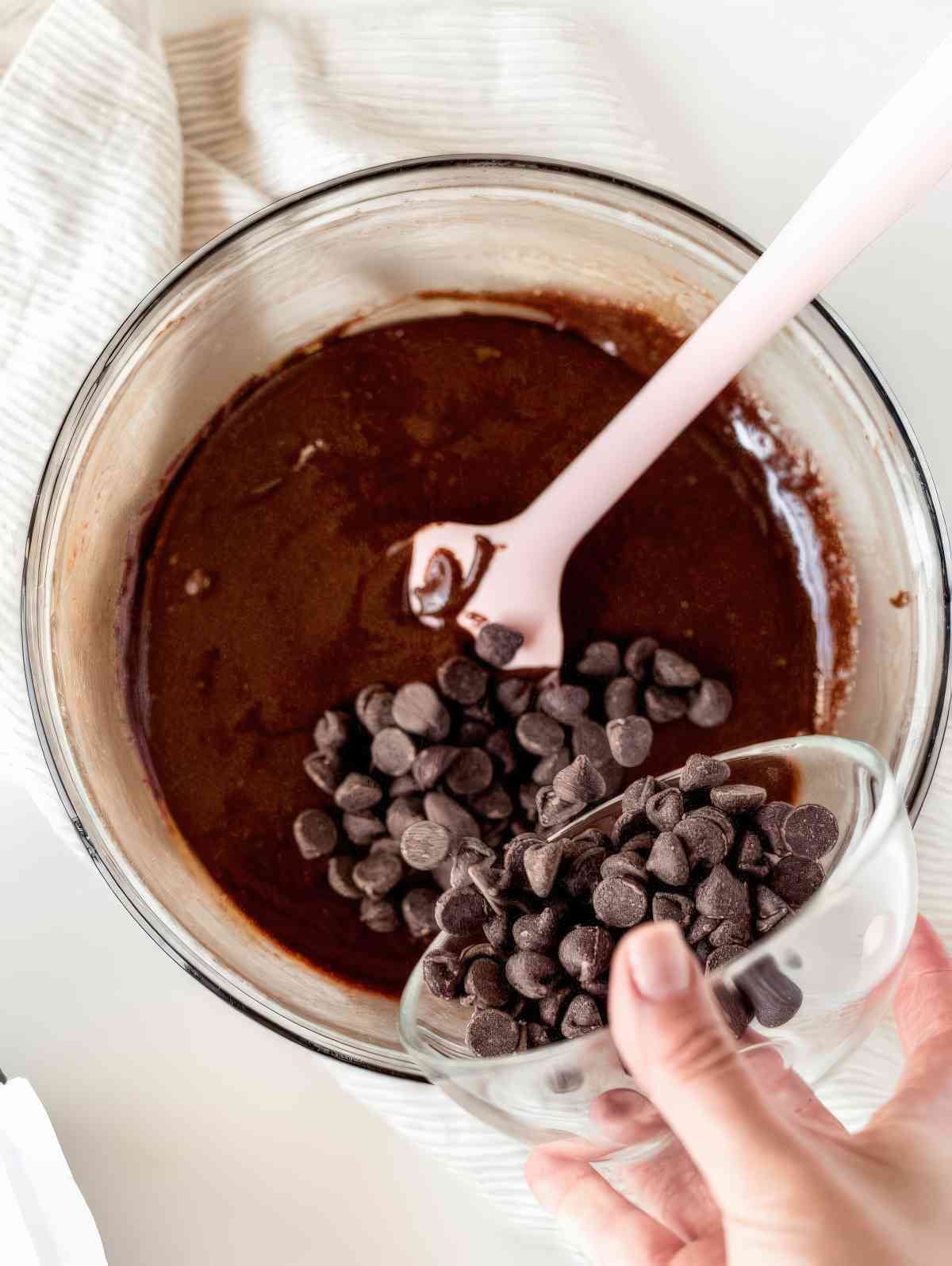 Adding chocolate chips to homemade brownie batter in a mixing bowl