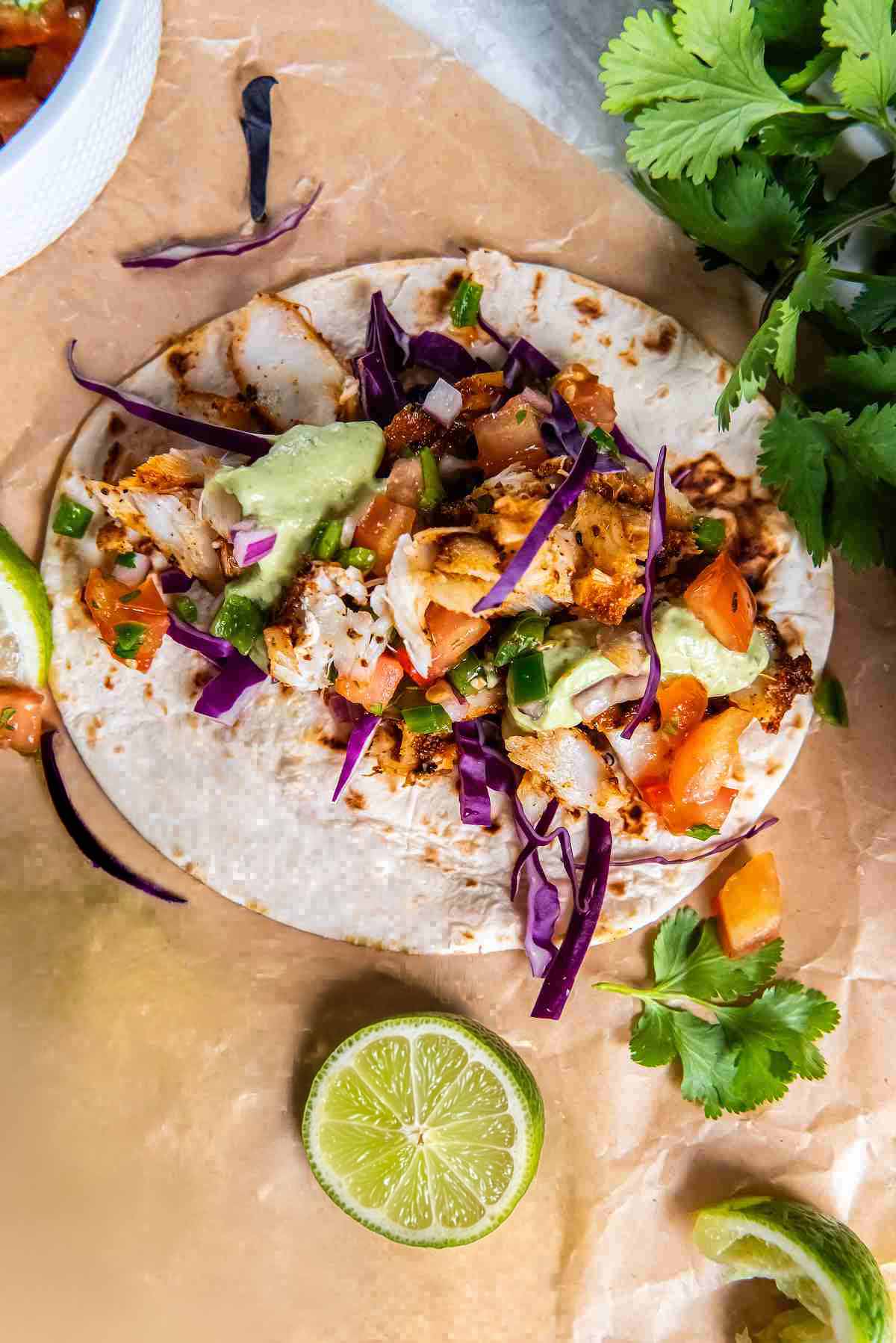 Assembling cod tacos with cabbage, pico de gallo, and avocado cilantro sauce
