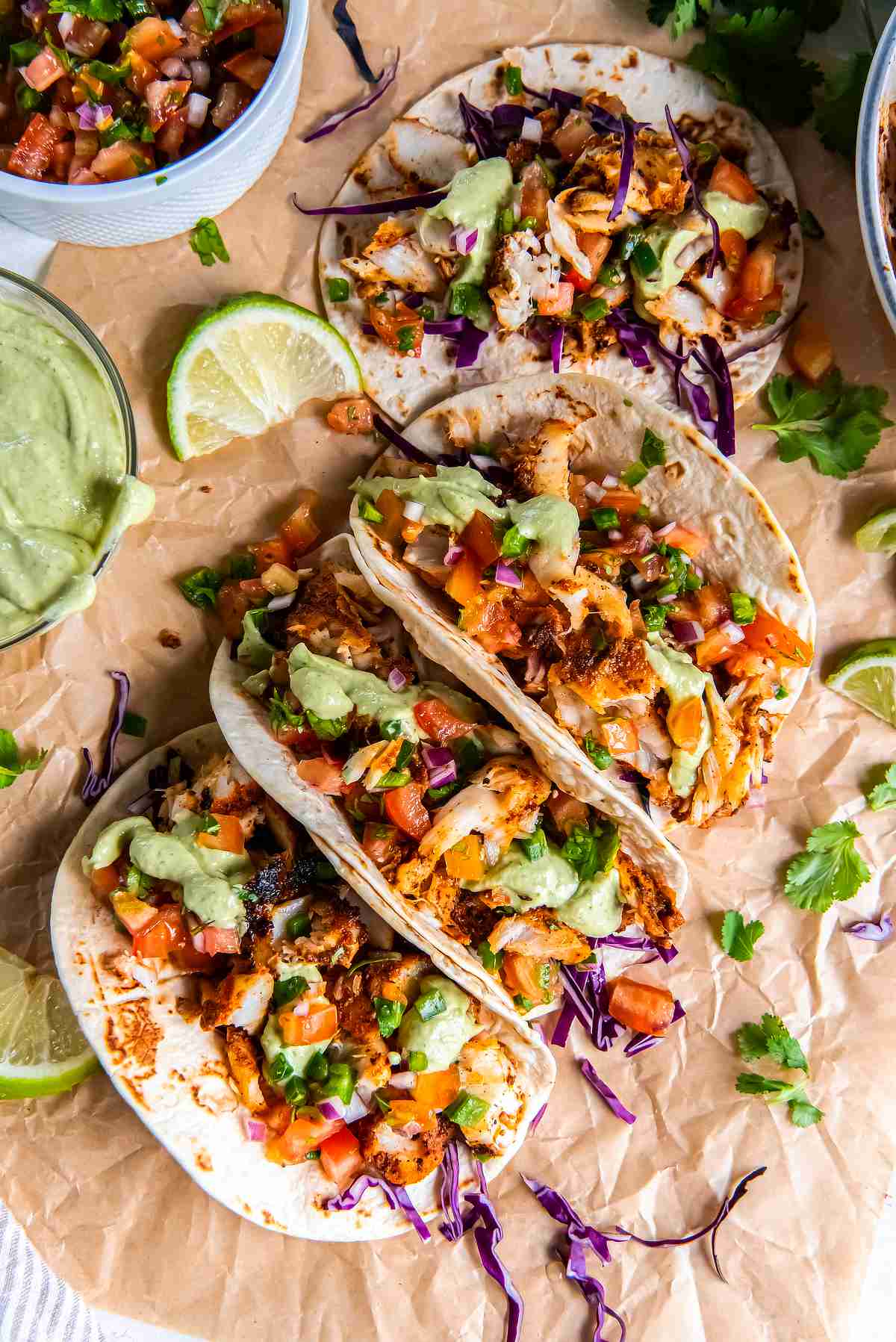 Blackened cod tacos topped with avocado cilantro sauce, pico de gallo, and cabbage slaw, served with lime wedges and salsa