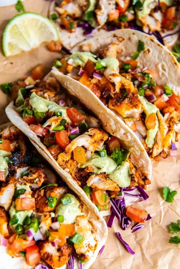 Close-up of blackened cod tacos with avocado cilantro sauce, fresh pico de gallo, and shredded cabbage