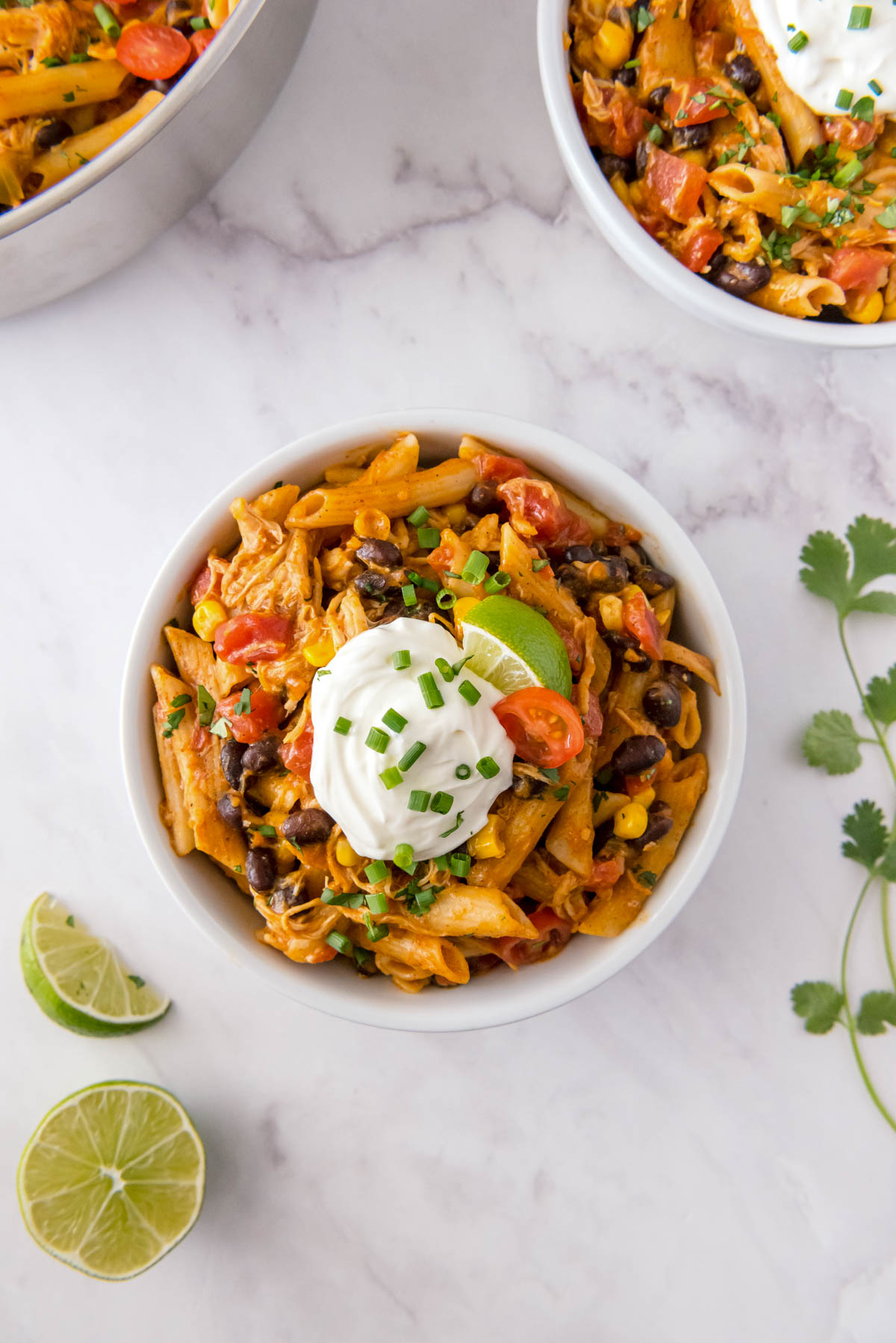 Chicken enchilada pasta served in a bowl topped with sour cream, lime wedge, black beans, corn and fresh cilantro