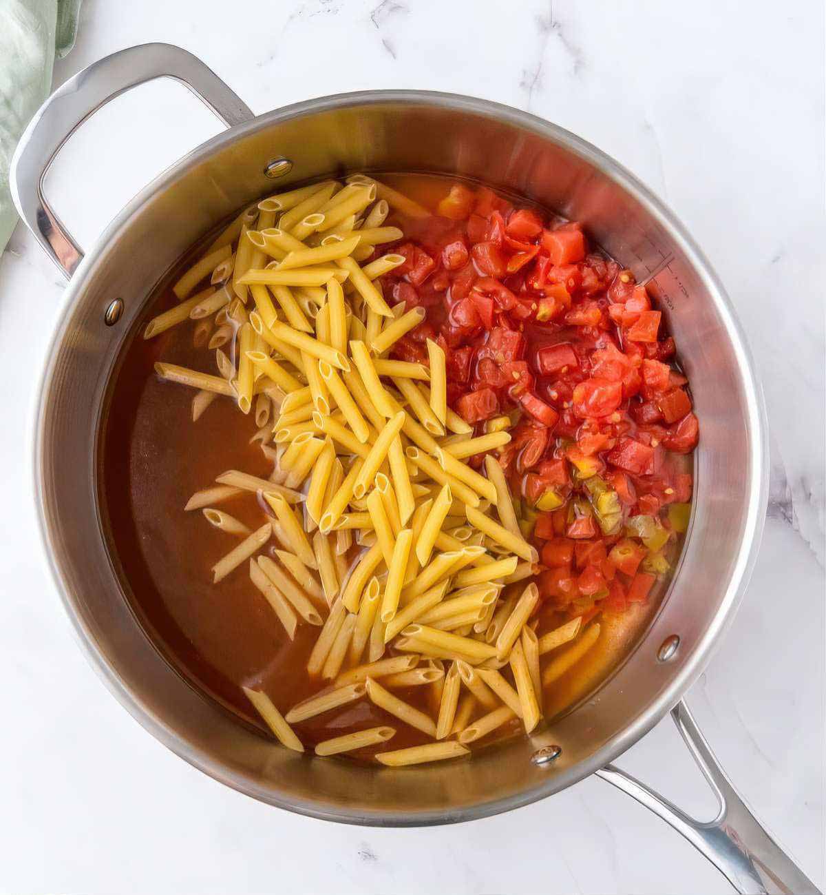 Pasta and diced tomatoes added to a skillet with enchilada sauce and broth to start chicken enchilada pasta