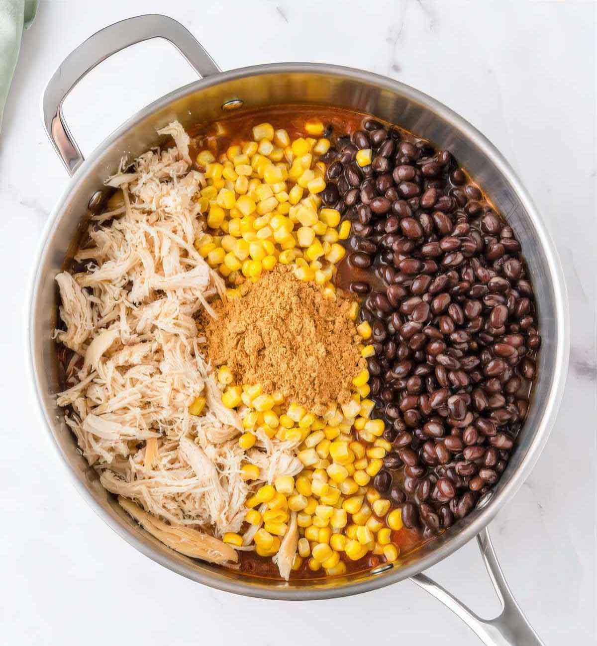 Shredded chicken, black beans, corn and taco seasoning added to skillet for chicken enchilada pasta