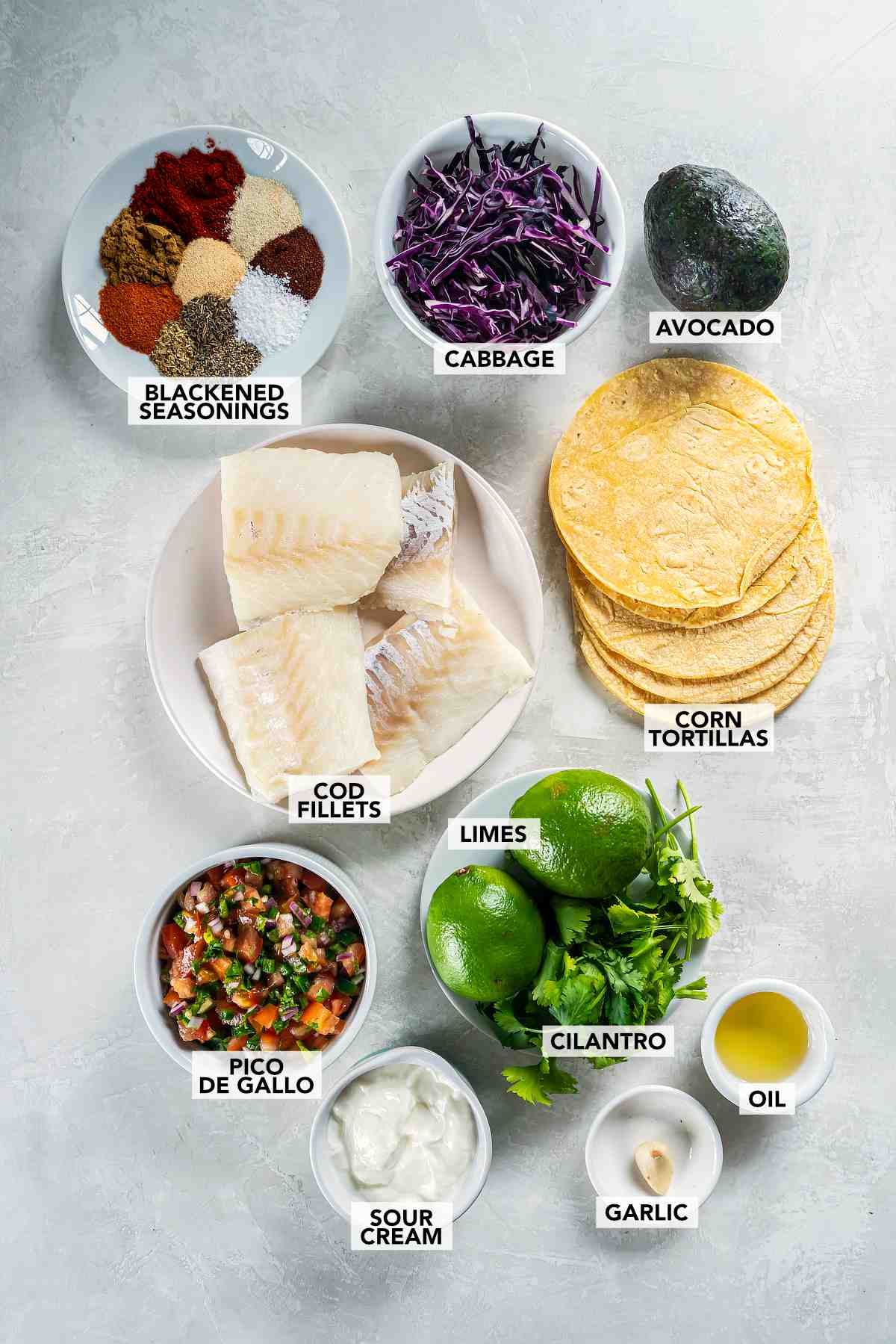 Ingredients for cod tacos including cod fillets, cabbage, tortillas, avocado, lime, pico de gallo, and blackened seasoning