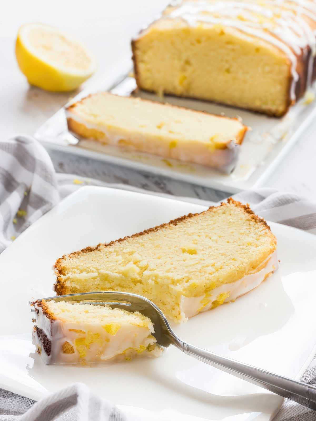 slice of lemon pound cake with thick lemon glaze on a plate with a fork showing soft texture