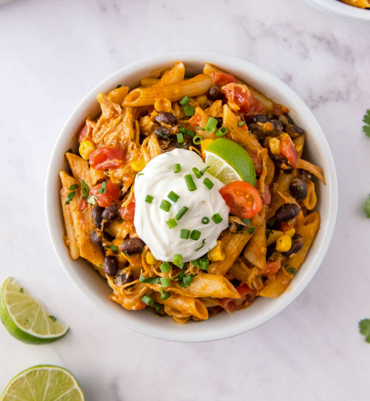 Close up of chicken enchilada pasta topped with sour cream, lime and green onions
